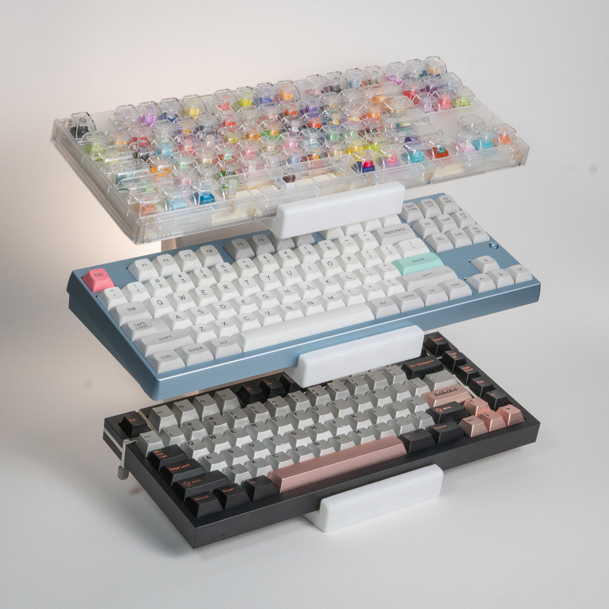White 3-tier keyboard stand holding a switch tester keyboard, a baby blue Neo80, and a Box75